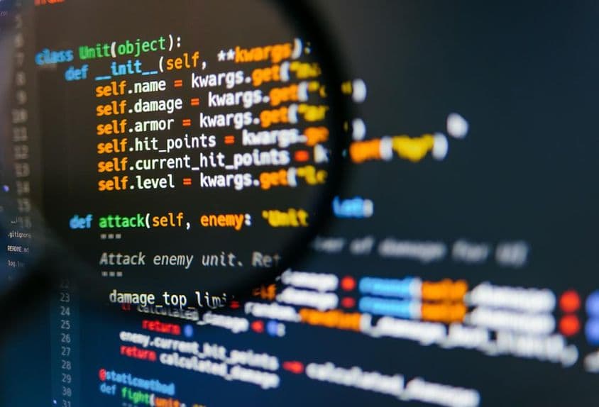 Programkód a számítógép kijelzőjén nagyítóval.