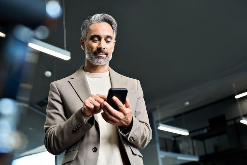 Középkorú üzletember egy telefont néz.