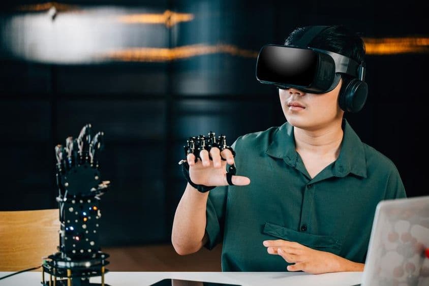 Egy ázsiai tinédzser VR-szemüveget visel és egy robotkar-projektet irányít.