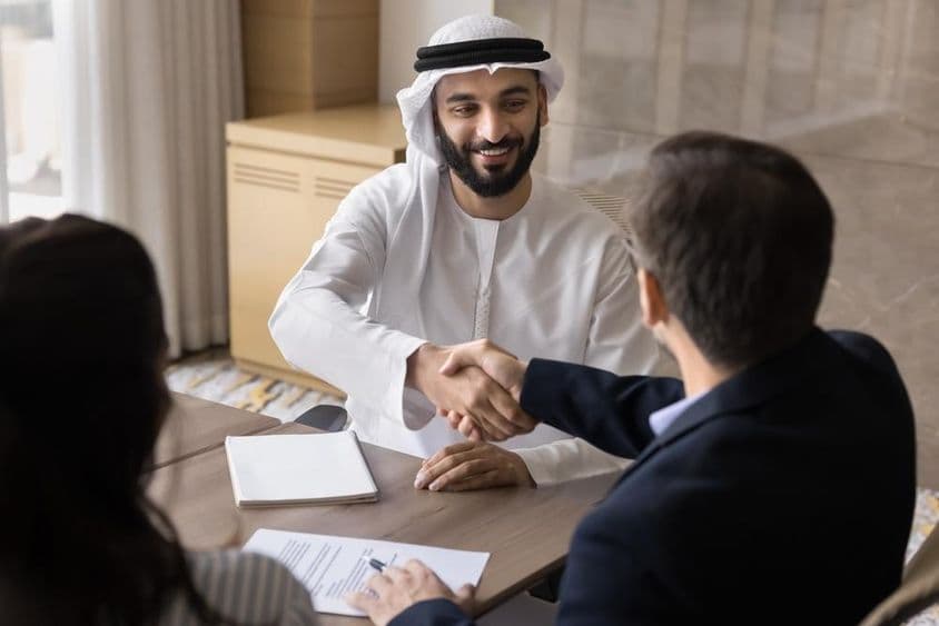 Boldog, magabiztos fiatal arab cégtulajdonos kezet ráz európai kollégákkal.