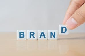 A férfi keze kockát tesz a "BRAND" szóval a fából készült asztalra.