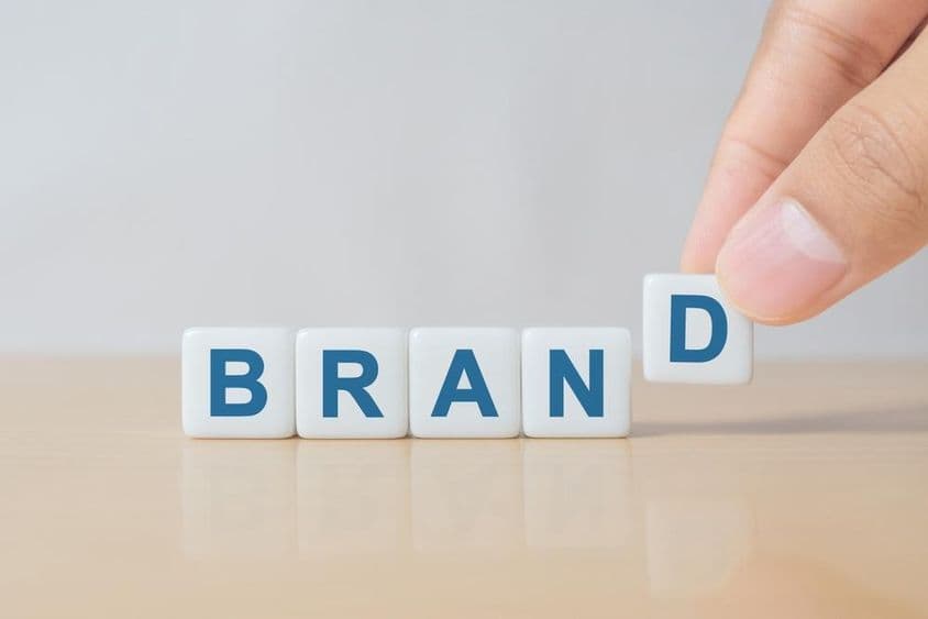 A férfi keze kockát tesz a "BRAND" szóval a fából készült asztalra.