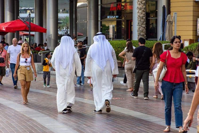 Két emirátusi férfi hátulról sétál a Dubai Mall előtt.